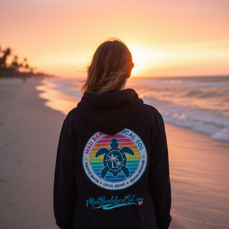 Woman on Florida beach at sunset wearing black Mad Beach Local Sol rainbow turtle crest hoodie, back view